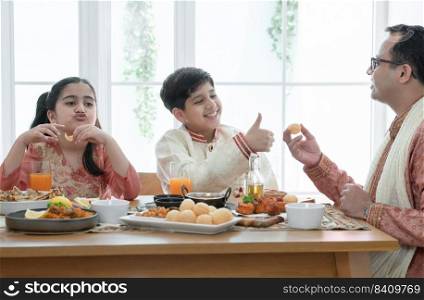Happy Indian family enjoy eating food with hands, South Asian father and children wear traditional clothes, sitting at dining table at home together. Indian culture lifestyle.