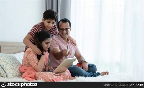 Happy indian family teenage boy son and girl with dad talking, teaching and doing daughter homework on laptop together at home, single father with children smiling and relaxing in bedroom, education.