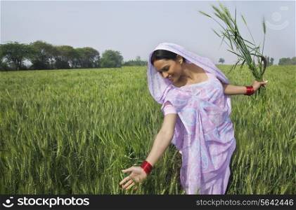Happy Indian female farm worker gliding through wheat field