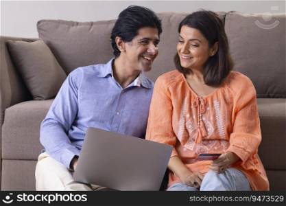 Happy Indian middle age couple shopping online through laptop using credit card