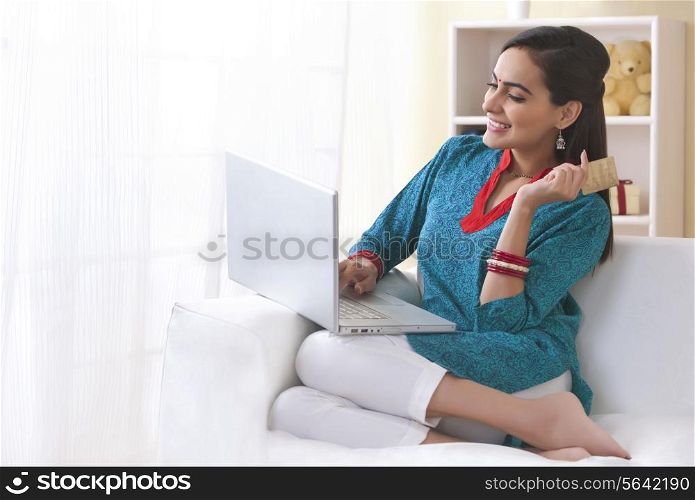 Happy Indian woman using laptop and credit card in living room
