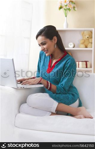 Happy Indian woman using laptop on sofa