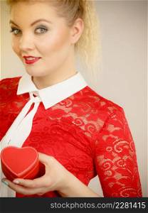 Happy joyful blonde woman with tied hair in pony tail holding valentines gift in heart shaped box. Female having beautiful make up.. Beautiful woman having heart box