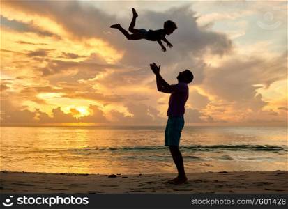 Happy joyful child, father throws up son in the air. Three year old toddler boy on beach with father at sunset. Summer family vacation at at Seychelles, Mahe.