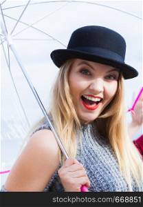 Happy joyful elegant adult woman in fedora hat holding transparent umbrella against sky. Weather forecasting concept.. Happy woman holding umbrella