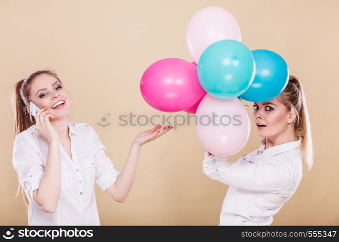 Happy joyful two girls having fun, playing with colorful balloons and talking on mobile phone. Holidays, celebration friendship and technology concept.. Two girls with mobile phone and balloons