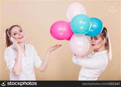 Happy joyful two girls having fun, playing with colorful balloons and talking on mobile phone. Holidays, celebration friendship and technology concept.. Two girls with mobile phone and balloons