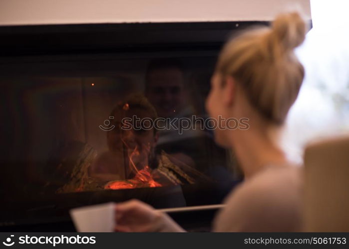 Happy joyful woman drinking cup of coffee relaxing at fireplace. Young beautiful girl with hot beverage heating warming up. autumn at home.