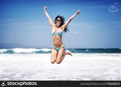 Happy joyful woman having fun on a beach, with pleasure jumping on a seashore, enjoying summer vacation on a tropical resort