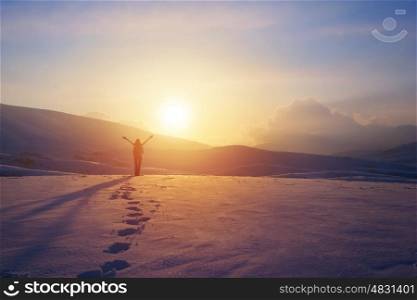 Happy joyful woman having fun outdoors in winter, standing on the mountains with raised up hands on the mountain covered with snow, enjoying beautiful sunset