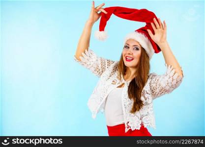 Happy joyful woman having fun, playing with santa claus red hat. Girl is ready for christmas holiday season. Blue background.. Joyful woman in christmas santa hat