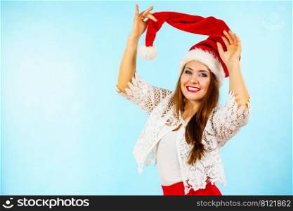 Happy joyful woman having fun, playing with santa claus red hat. Girl is ready for christmas holiday season. Blue background.. Joyful woman in christmas santa hat
