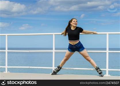 Happy joyful young woman wearing roller skates fooling around stretching her legs. Female being sporty having fun during summer time near sea.. Happy crazy woman wearing roller skates