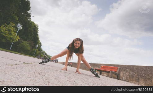 Happy joyful young woman wearing roller skates fooling around stretching her legs. Female being sporty having fun during summer time near sea.. Happy crazy woman wearing roller skates