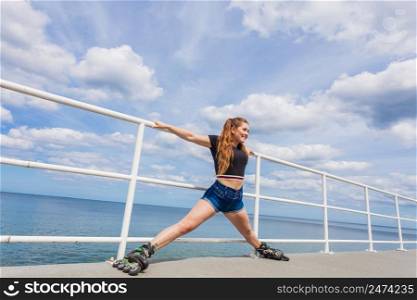 Happy joyful young woman wearing roller skates on sea. Girl having fun during summer time.. Joyful teen girl wearing roller skates