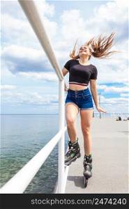 Happy joyful young woman wearing roller skates on sea. Girl having fun during summer time.. Joyful teen girl wearing roller skates