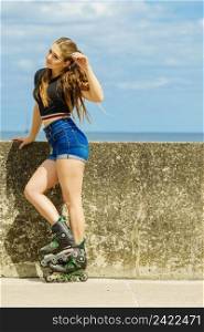 Happy joyful young woman wearing roller skates relaxing after long ride. Female being sporty having fun during summer time near sea.. Happy young woman wearing roller skates