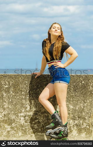 Happy joyful young woman wearing roller skates relaxing after long ride. Female being sporty having fun during summer time near sea.. Happy young woman wearing roller skates