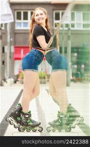 Happy joyful young woman wearing roller skates riding in town next to mirror wall. Female being sporty having fun during summer time.. Woman posing outdoor with roller skates