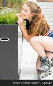 Happy joyful young woman wearing roller skates riding in town smelling flowers. Female being sporty having fun during summer time.. Young woman riding roller skates