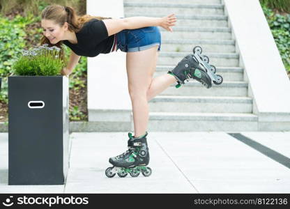 Happy joyful young woman wearing roller skates riding in town smelling flowers. Female being sporty having fun during summer time.. Young woman riding roller skates