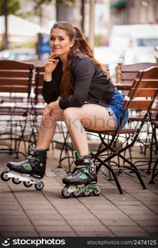 Happy joyful young woman wearing roller skates sitting in town. Female being sporty having fun during summer time.. Young woman riding roller skates