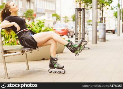 Happy joyful young woman wearing roller skates sitting in town. Female being sporty having fun during summer time.. Young woman sitting wearing roller skates