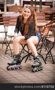 Happy joyful young woman wearing roller skates sitting in town. Female being sporty having fun during summer time.. Young woman riding roller skates