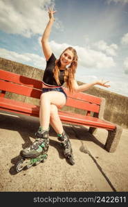 Happy joyful young woman wearing roller skates sitting on bench enjoying herself. Female being sporty having fun during summer time.. Young woman riding roller skates