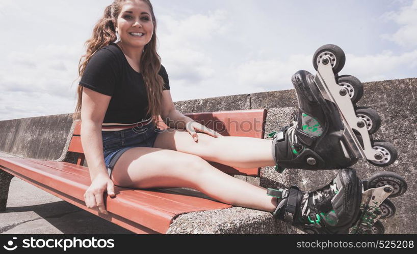 Happy joyful young woman wearing roller skates sitting on bench enjoying herself. Female being sporty having fun during summer time.. Young woman riding roller skates