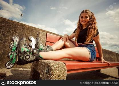 Happy joyful young woman wearing roller skates sitting on bench enjoying herself. Female being sporty having fun during summer time.. Young woman riding roller skates