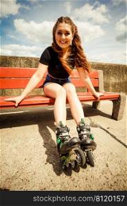Happy joyful young woman wearing roller skates sitting on bench enjoying herself. Female being sporty having fun during summer time.. Young woman riding roller skates