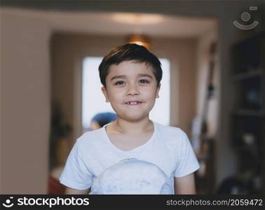 Happy kid boy standing in living room looking out with smiling face, Indoor portrait Cute child wearing white T- Shirt holding fluffy toy playing and relaxing at home in Evening