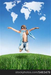 Happy kid dressed as a pilot jumping in green field against blue sky. Summer vacation concept