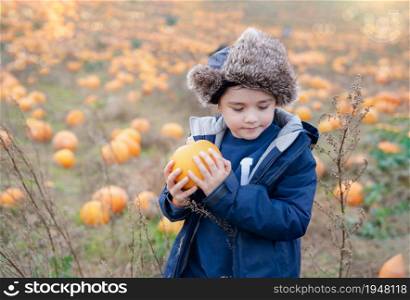 Happy kid holding pumpkin, Cute boy having fun playing outdoor in Autumn field. Smiling Child playing outside for trick or teat on halloween. Harvest or Thanksgiving Festive season in October
