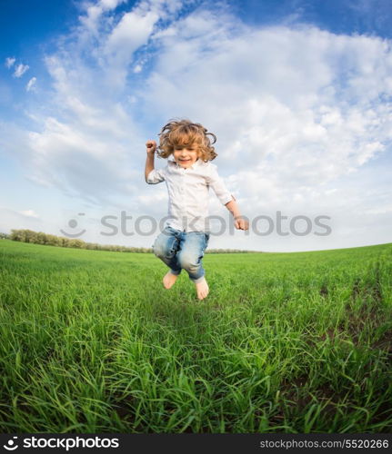 Happy kid jumping in green field against blue sky. Summer vacation concept