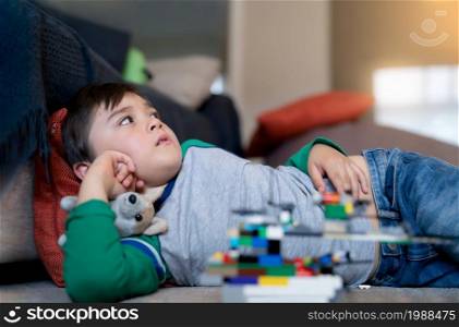Happy kid lying on floor watching TV, Cute young boy playing with toys in living room after school, Positive child relaxing at home