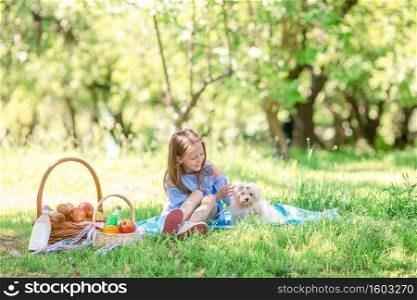 Happy kid on picnic plays with white puppy on green grass in spring cherry garden. Little kid with puppy on picnic in the park