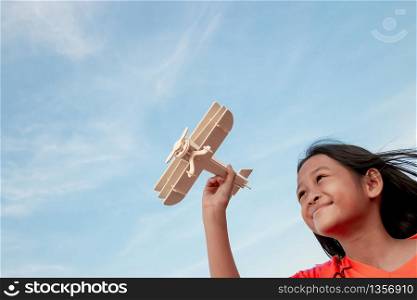 Happy kid playing with toy wooden airplane against sunset sky background.
