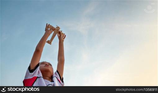 Happy kid playing with toy wooden airplane against sunset sky background.