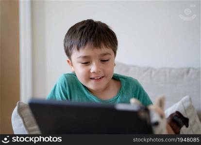 Happy Kid sitting on sofa having fun taking with his class friends on tablet, Child boy studying online on digital tablet, new normal lifestyle with learning online, Distance education
