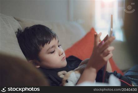 Happy kid watching cartoon on tablet, Candid shot cute boy playing game online with friends on internet in evening, A Child sitting on sofa relaxing at home on weekend