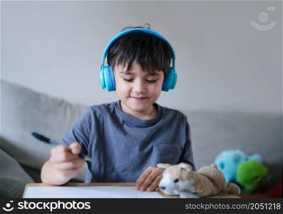 Happy kid wearing headphones listening to music while drawing on paper, Indoors portrait Cute child boy enjoy creative activity at home on weekend.