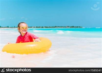 Happy kid with inflatable rubber ring on the beach in waves. Adorable little girl having fun on the beach