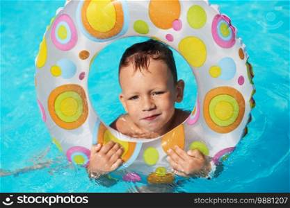 Happy kid with swim ring playing in blue water of swimming pool. Little boy learning to swim. Summer vacations concept. Cute boy swimming in pool water. Child splashing and having fun in swimming pool