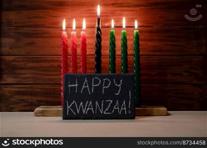 Happy Kwanzaa. African American holiday. Seven candles red, black and green on wooden background. Symbols of African heritage. Congratulatory inscription on chalk board.. Happy Kwanzaa. African American holiday. Seven candles red, black and green