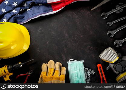 Happy Labor Day. Several engineer constructor work tools, medical face mask protective and American flag with copy space black dark background, American workforce during breakout coronavirus concept