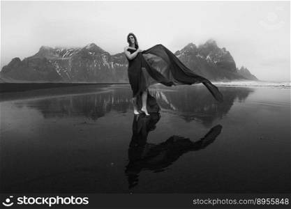 Happy lady wrapped with chiffon on beach monochrome scenic photography. Picture of person with hills on background. High quality wallpaper. Photo concept for ads, travel blog, magazine, article. Happy lady wrapped with chiffon on beach monochrome scenic photography