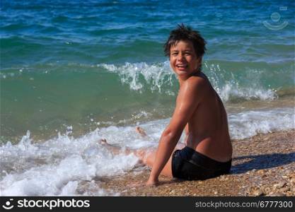 happy laughing boy of twelve sitting on the sea beach