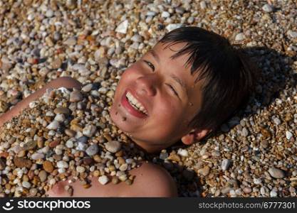 happy laughing boy of twelve, sprinkled with pebbles on the beach